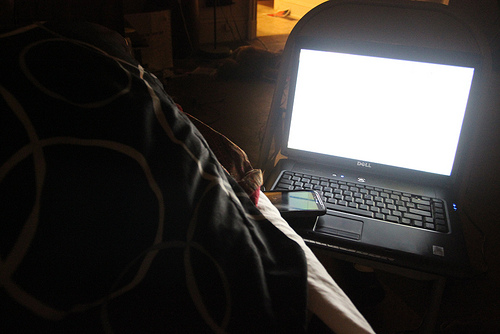 a dark room with a laptop screen glowing in a bed