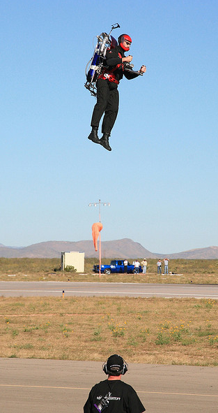 picture of lone man in airfield hovering about 20 feet above the ground using a two cylinder jet back pack