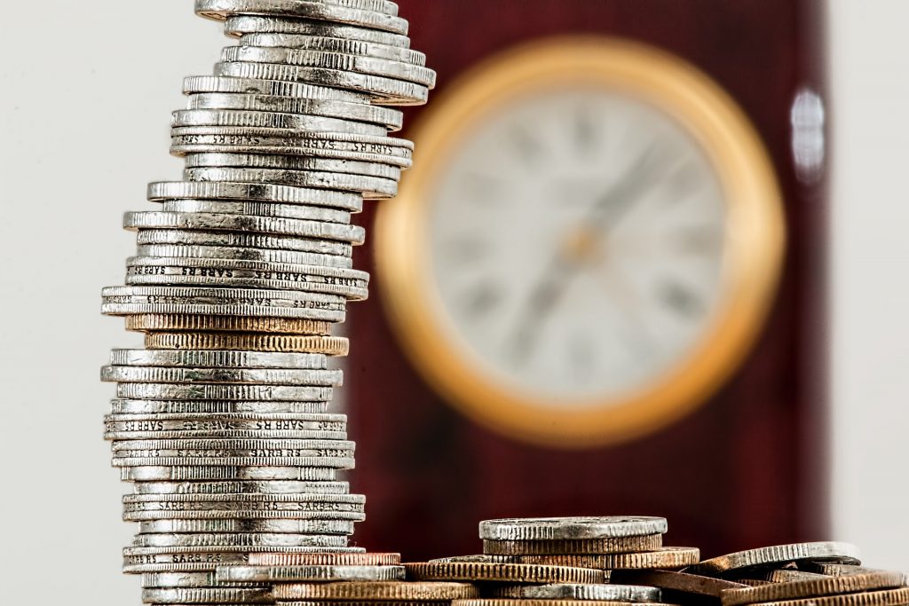 a tall, single pile of coins set against a blurred clock in the background