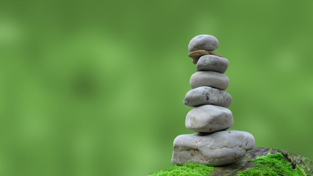 a pile of balanced smooth stones arranged in bigger to smaller sizes vertically, from the ground up. Set against a blurred nature (green) background