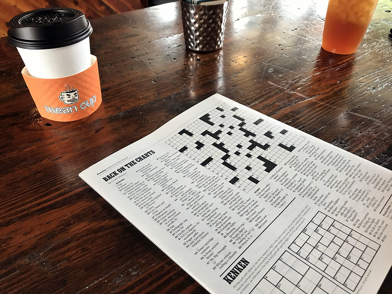 a newspaper opened to the crossword on a wood table in a cafe