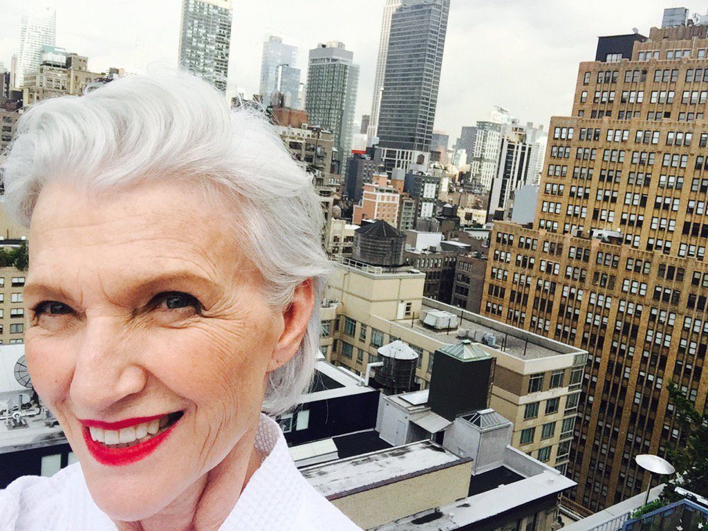 Picture of 70-something white female model with white short hair on the top of a building in a city with the skyline behind her. 
