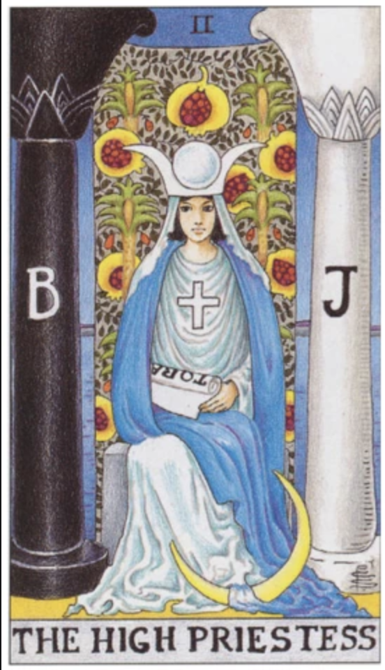 A white woman with dark hair sits on a religious throne surrounded by draperies and many religious symbols of every major world religion. She holds a scroll. There is a black column to her right emblazoned with a B and a white column to her left emblazoned with a J.