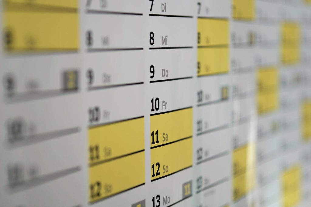 a close up of a very dense wall calendar month view with weekends highlighted in yellow. Black print. Abbreviated days of the week are in another language, maybe Portuguese