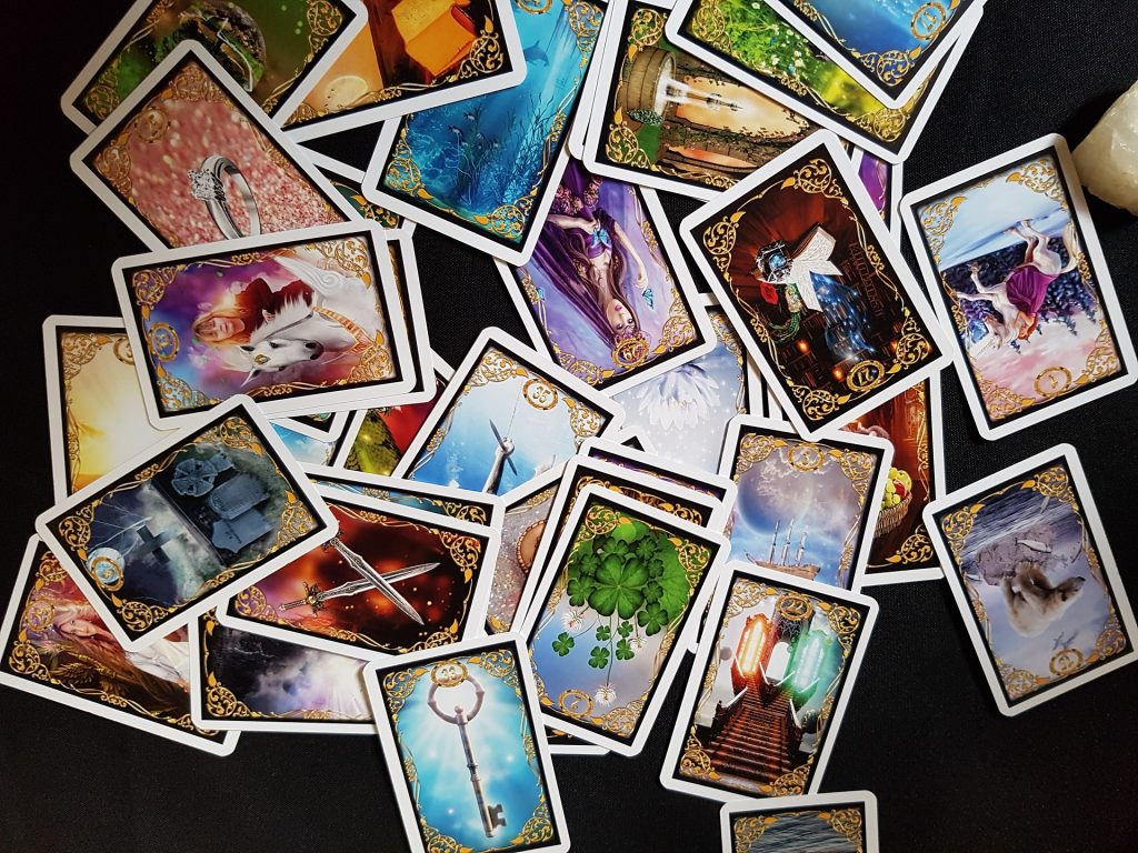 a scattered deck of colorful tarot cards with faces up against a black background